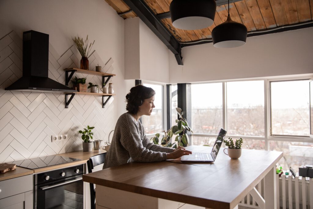 Frau mit Headset sitzt an Küchentisch und tippt auf ihrem Laptop 